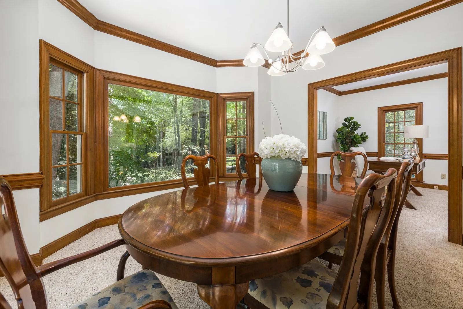 Spacious dining room featuring wood trim, a chandelier, and garden views through large windows.